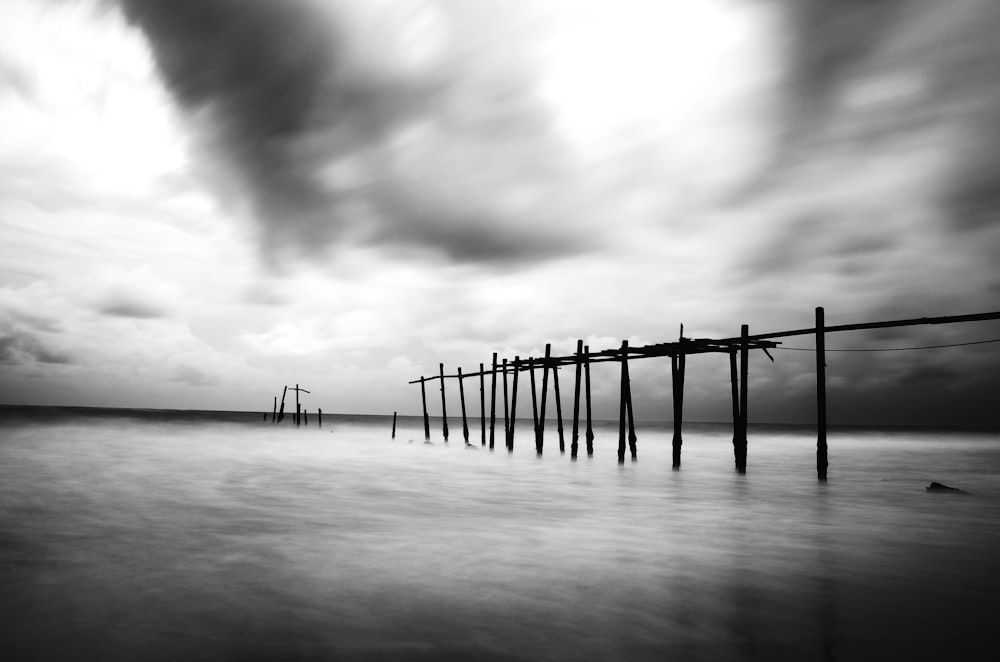 a black and white photo of a pier on a cloudy day