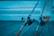 Two fishing rods are positioned on a wooden surface, extending into the frame from the right. The background features softly focused steps, and the color palette includes shades of blue, giving the scene a calm, serene feel.