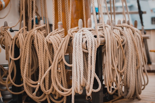 Several coiled ropes are neatly arranged and hung along a wooden railing or structure, possibly on a ship. The ropes are thick and uniformly coiled, indicating organization and order.
