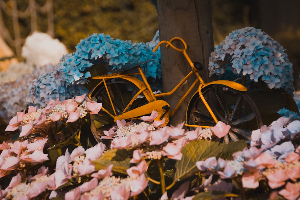 a yellow bicycle parked next to a bunch of flowers