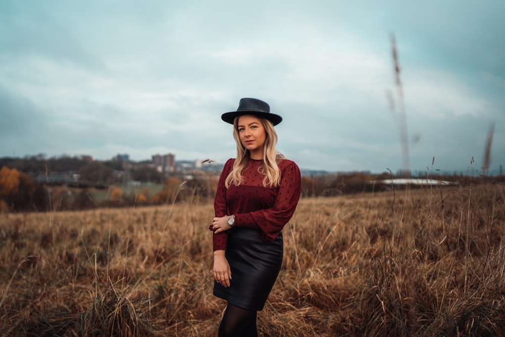 woman in maroon long-sleeved blouse and black miniskirt standing on brown grass fields during daytime