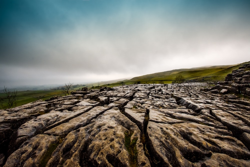 rock formation near grass field under cloudy sky