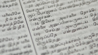 Close-up of hands editing a printed Sinhala manuscript with a red pen.