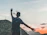 A smiling traveler with a backpack standing on a scenic overlook at sunrise.