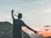 A smiling young traveler standing on a mountain ridge at sunset, backpack on, soaking in the view.