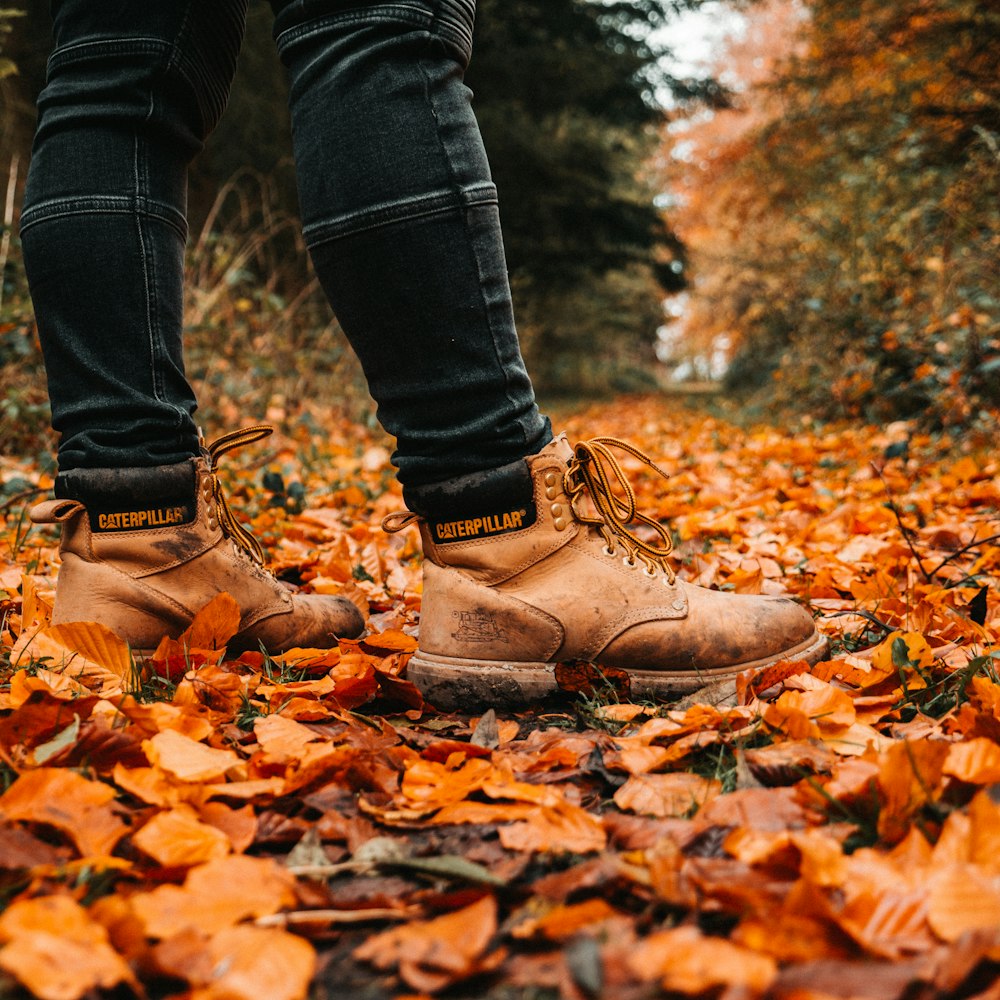 man wearing brown Caterpillar leather work boots standing on ground with leaves