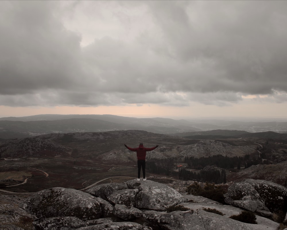 person standing on rock spreading their arms facing the mountains