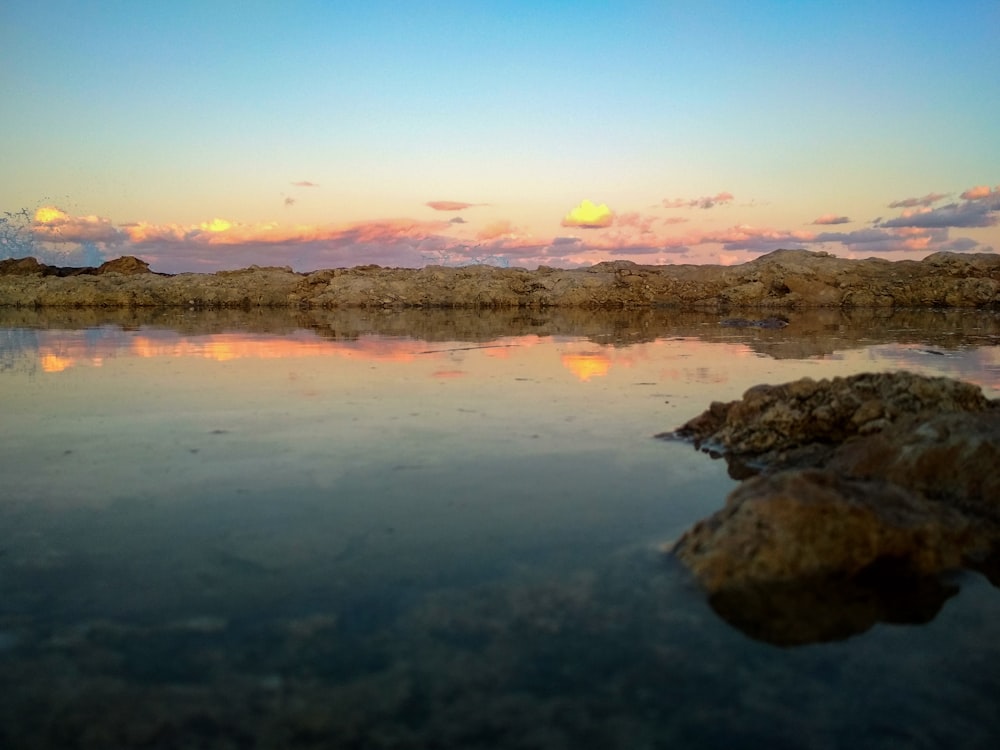 rock formations on body of water viewing mountain under orange and blue sky