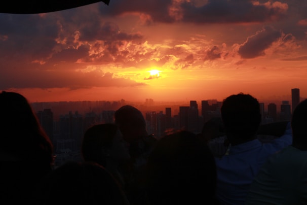 Sunset over the city skyline with silhouettes of people taking photos along the waterfront.