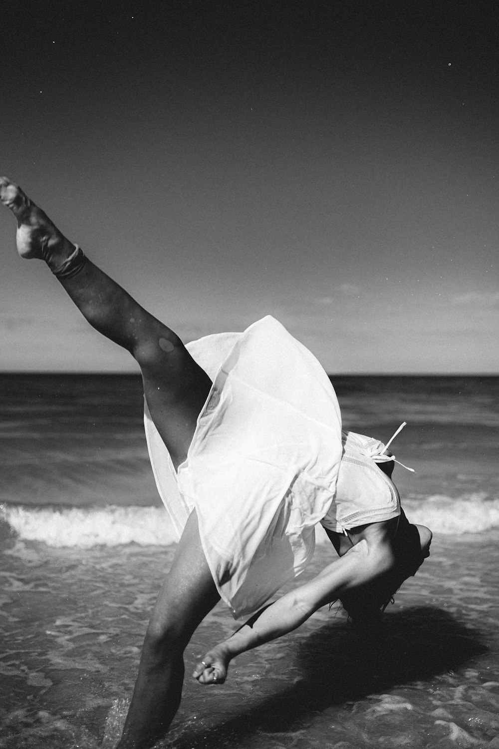 grayscale photography of woman dancing near seashore