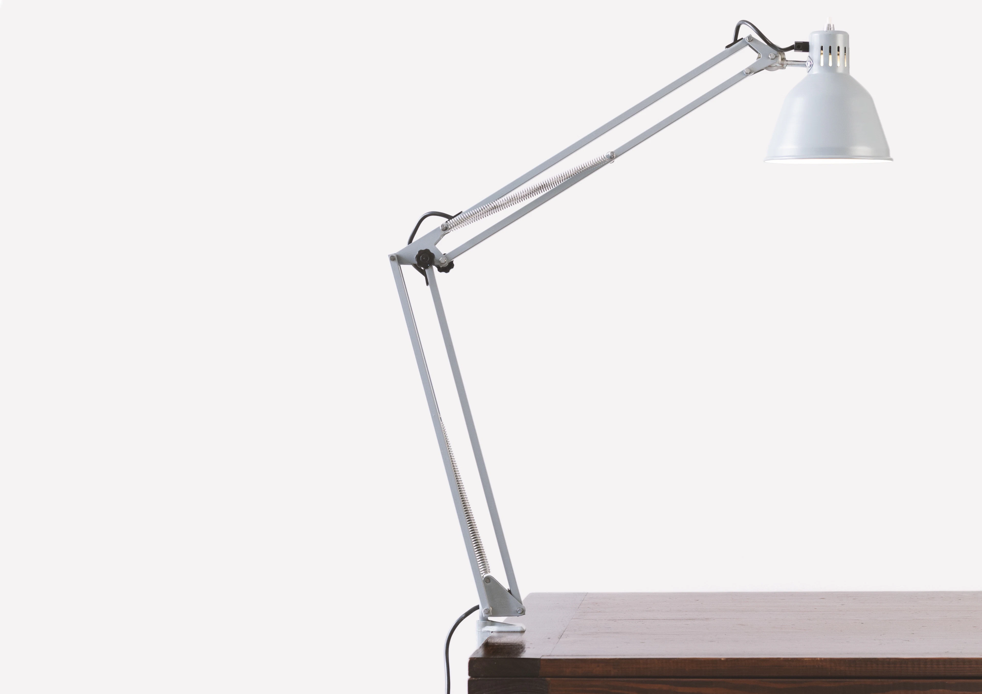 A white balanced-arm architect desk lamp against a pale wall