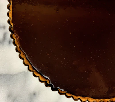 Close-up of a beautifully decorated chocolate tart with gold accents on a cream background.