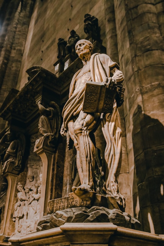 low-angle photography of man carrying a book statue in Duomo di Milano Italy