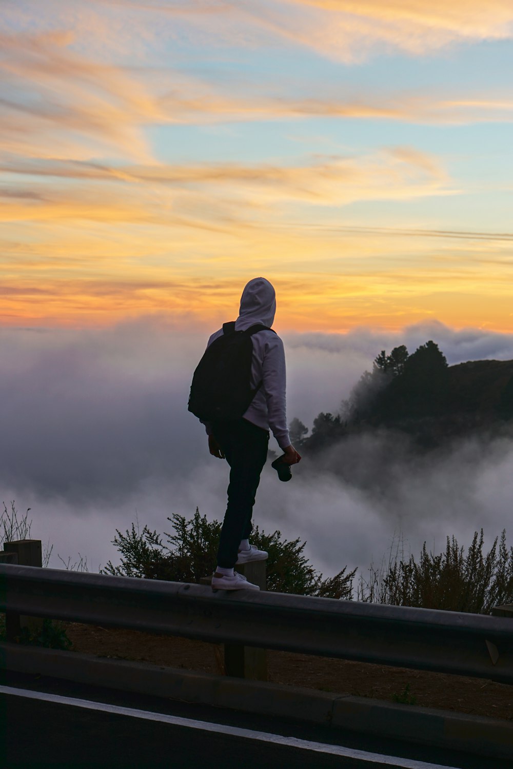 man standing on a fence overlooking sea of clouds