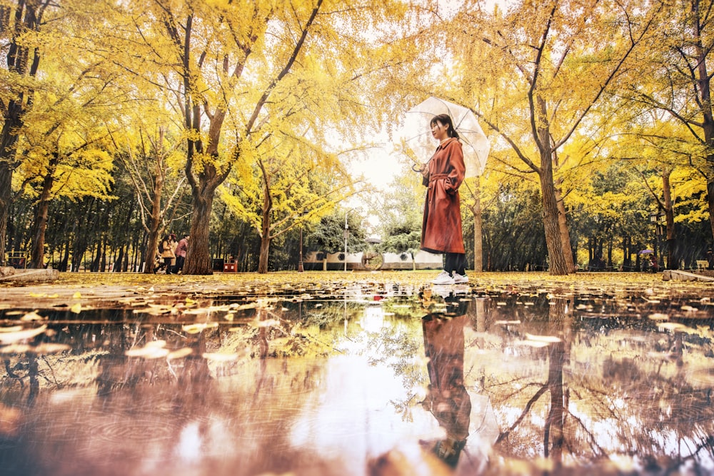 woman wearing red long-sleeved dress standing near wet pathway surrounded with green trees