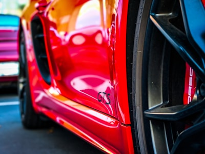 A close-up view of a red sports car prominently displaying the GTS badge on its side. Part of the wheel is visible, emphasizing the sleek design and detailing typical of high-performance vehicles.