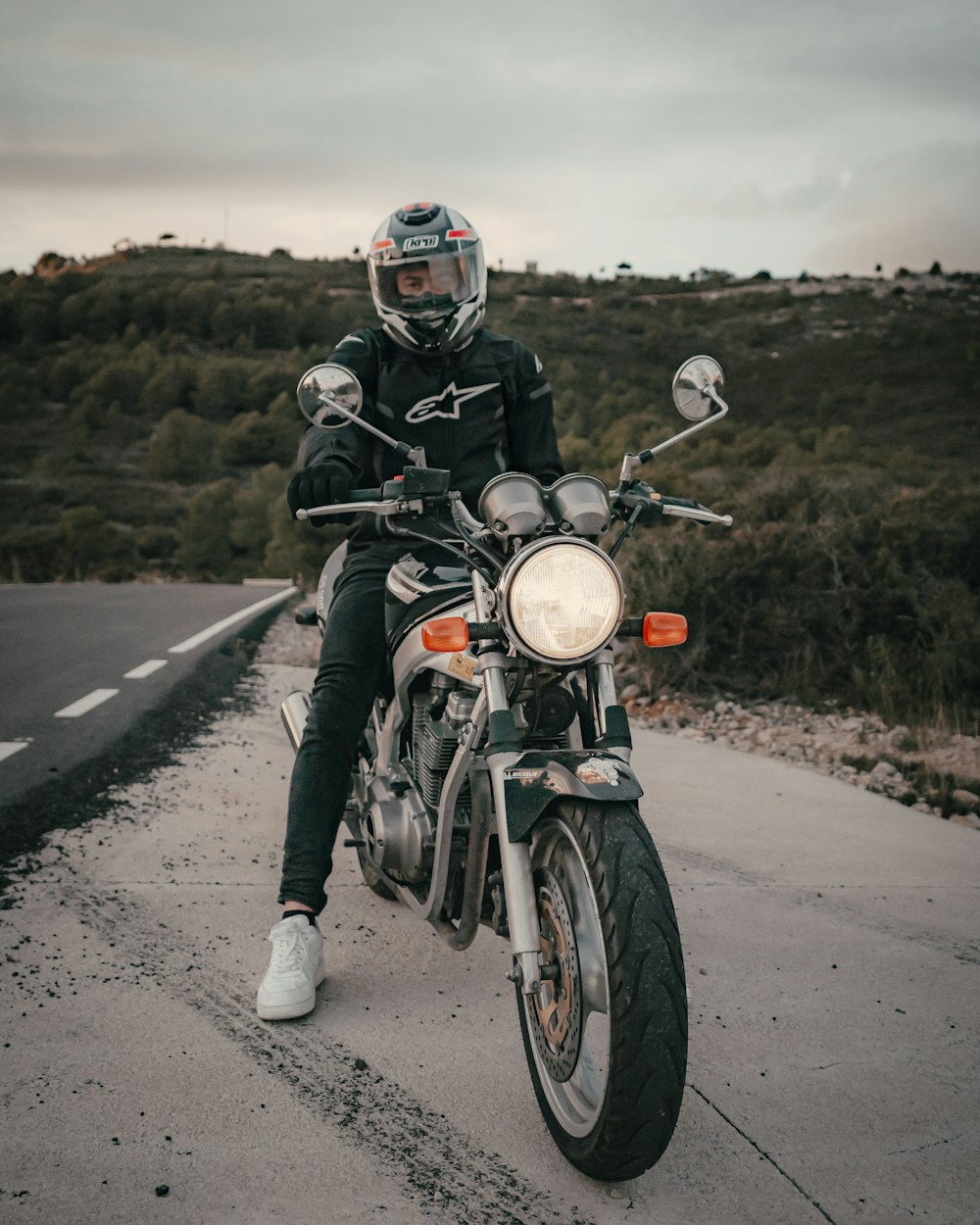 man wearing black and white Alpinestar jacket riding motorcycle near road