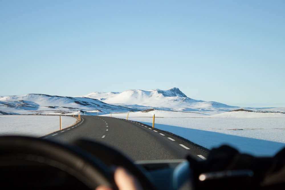 person riding vehicle on paved road between snow field