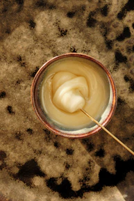Close-up of hands gently stirring honey infused with herbs in a small ceramic bowl.