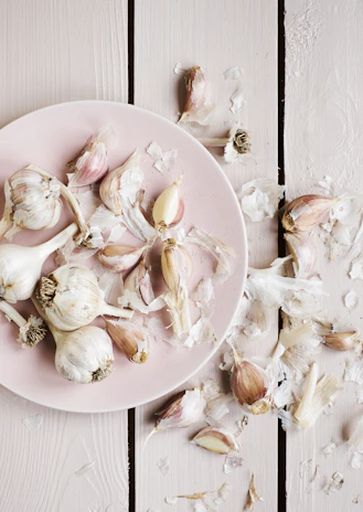 Fresh garlic bulbs and garlic powder arranged on a wooden kitchen table with natural light.