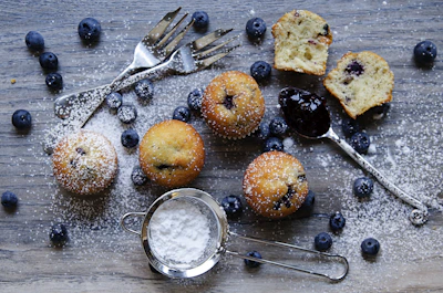 A rustic wooden table displaying freshly baked whole grain muffins with blueberries.