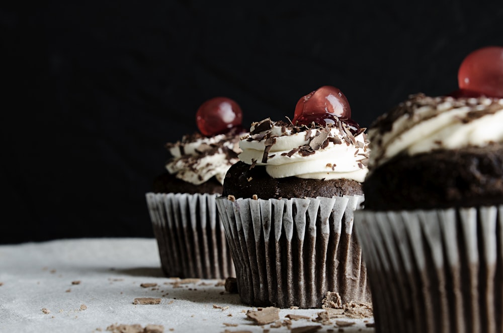 three chocolate cupcakes with cherries