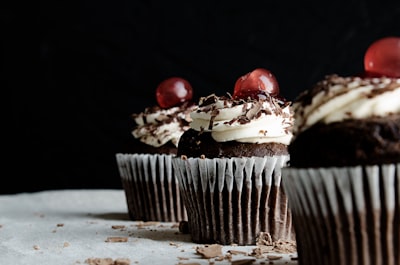 three chocolate cupcakes with cherries cake teams background