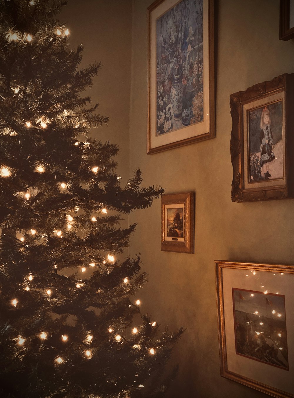 Christmas tree with turned on mini string lights near wall of pictures