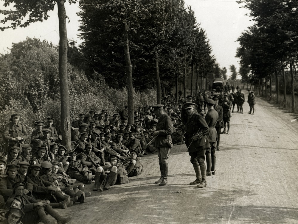 Fotografía en escala de grises de soldados sentados cerca de la carretera y otros de pie
