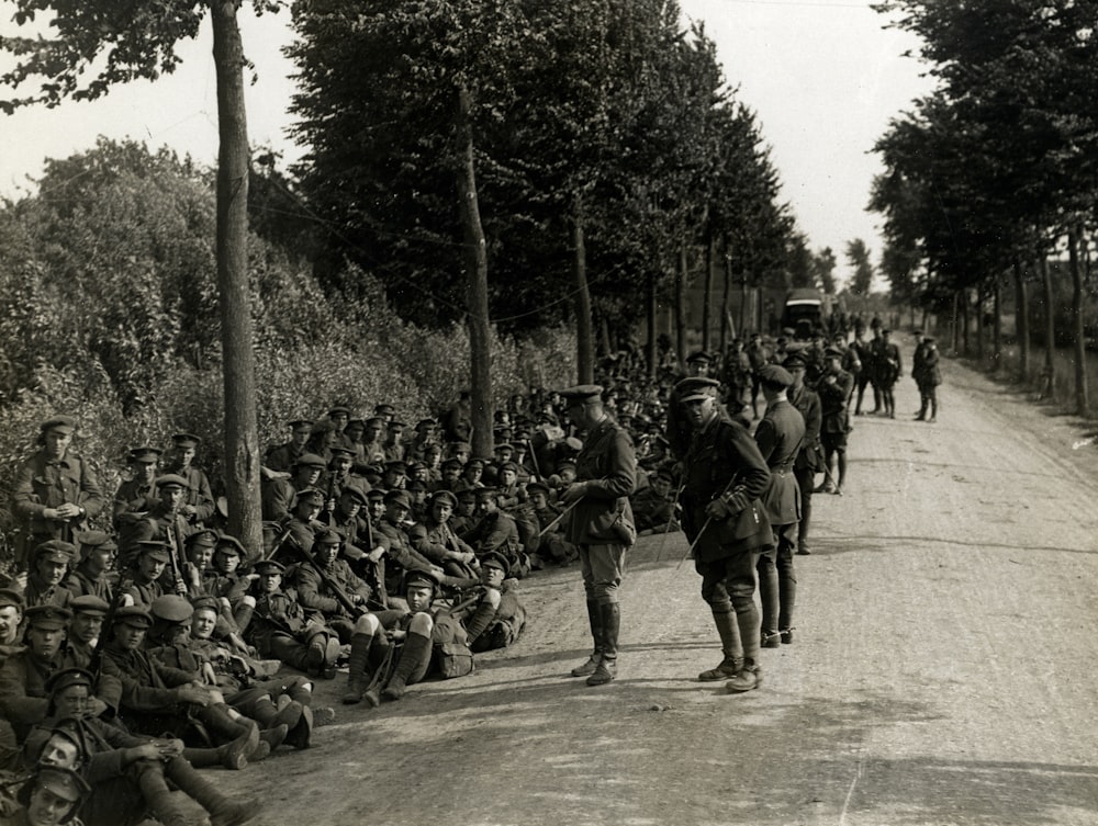 grayscale photography of soldiers sitting near road and others are standing