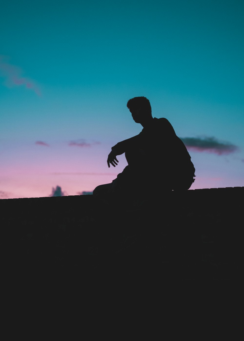 Silhouettenfotografie eines Mannes, der unter einem ruhigen blauen Himmel sitzt