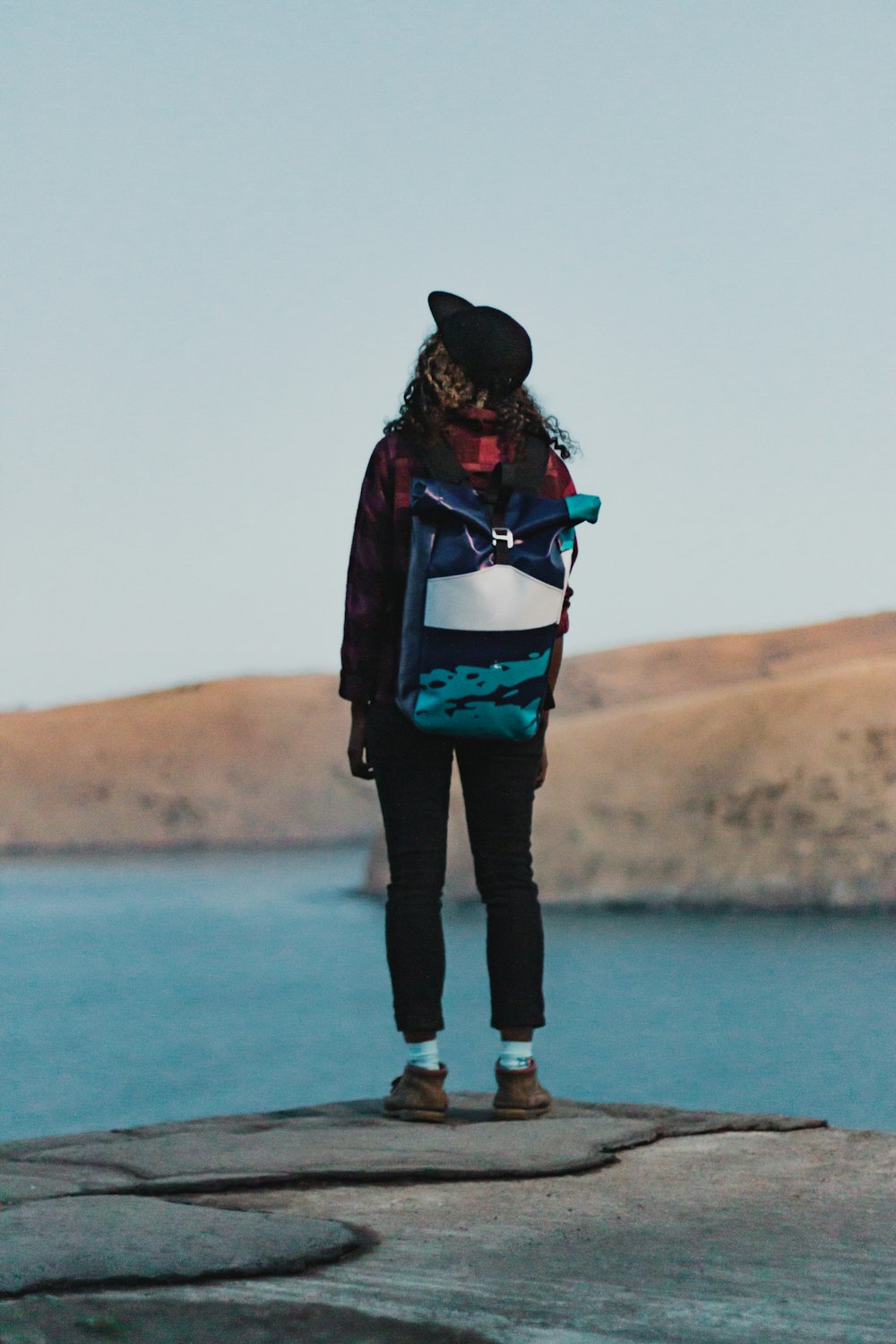 woman standing on a cliff facing body of water