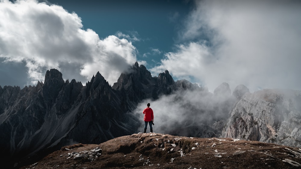 person standing on cliff viewing mountain under white and blue sky