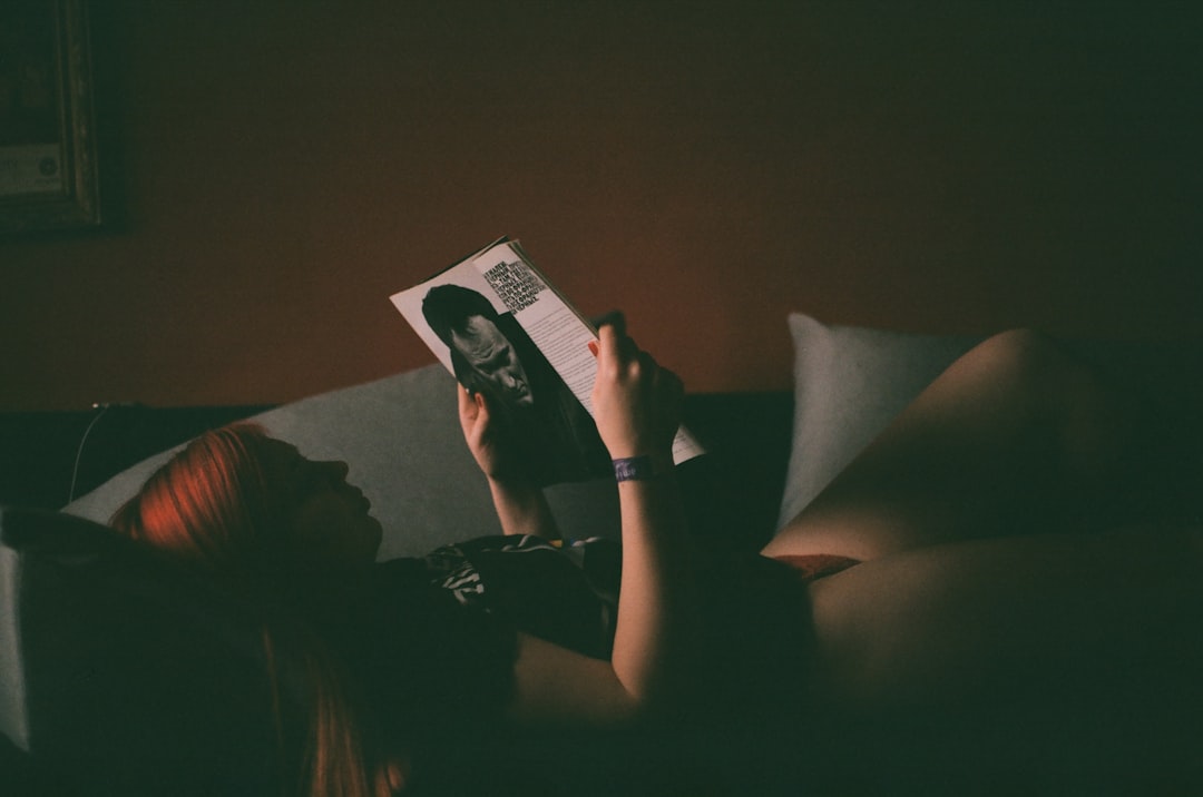 woman holding magazine lying on sofa