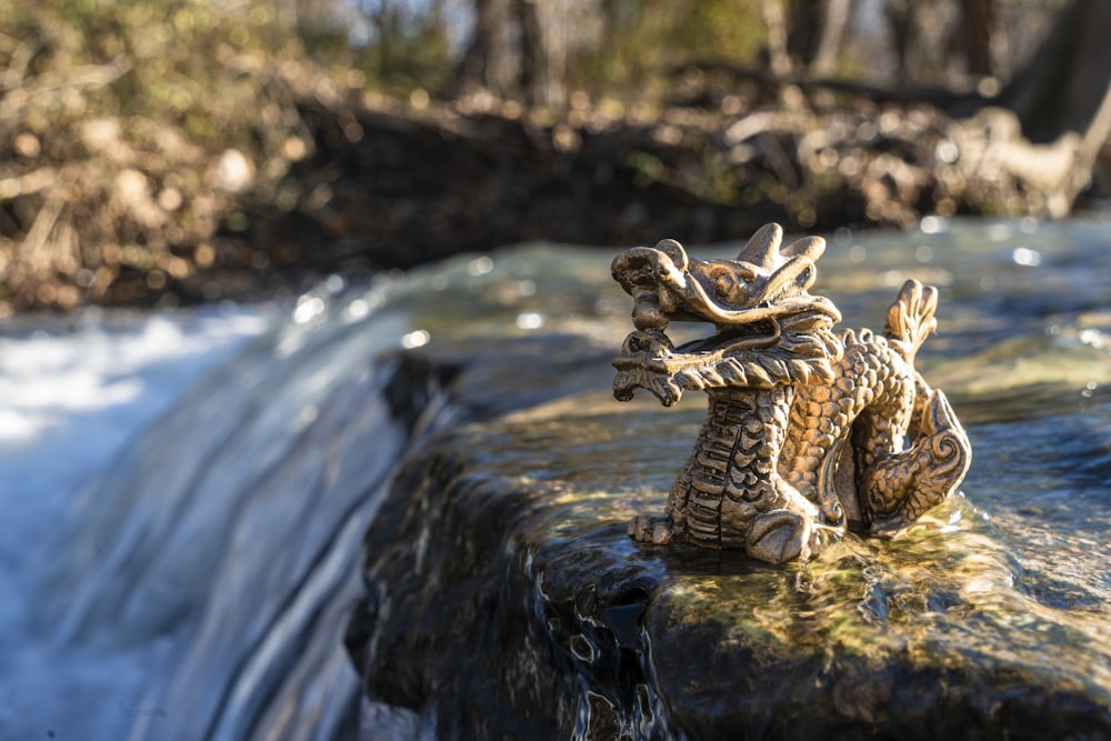 Goldfarbene Drachenfigur auf Felsbrocken am Fluss