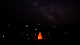 A softly glowing flame surrounded by delicate cosmic starfield and ethereal line art in midnight indigo and soft gold tones.