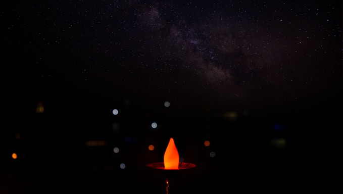 A softly glowing flame surrounded by delicate cosmic starfield and ethereal line art in midnight indigo and soft gold tones.