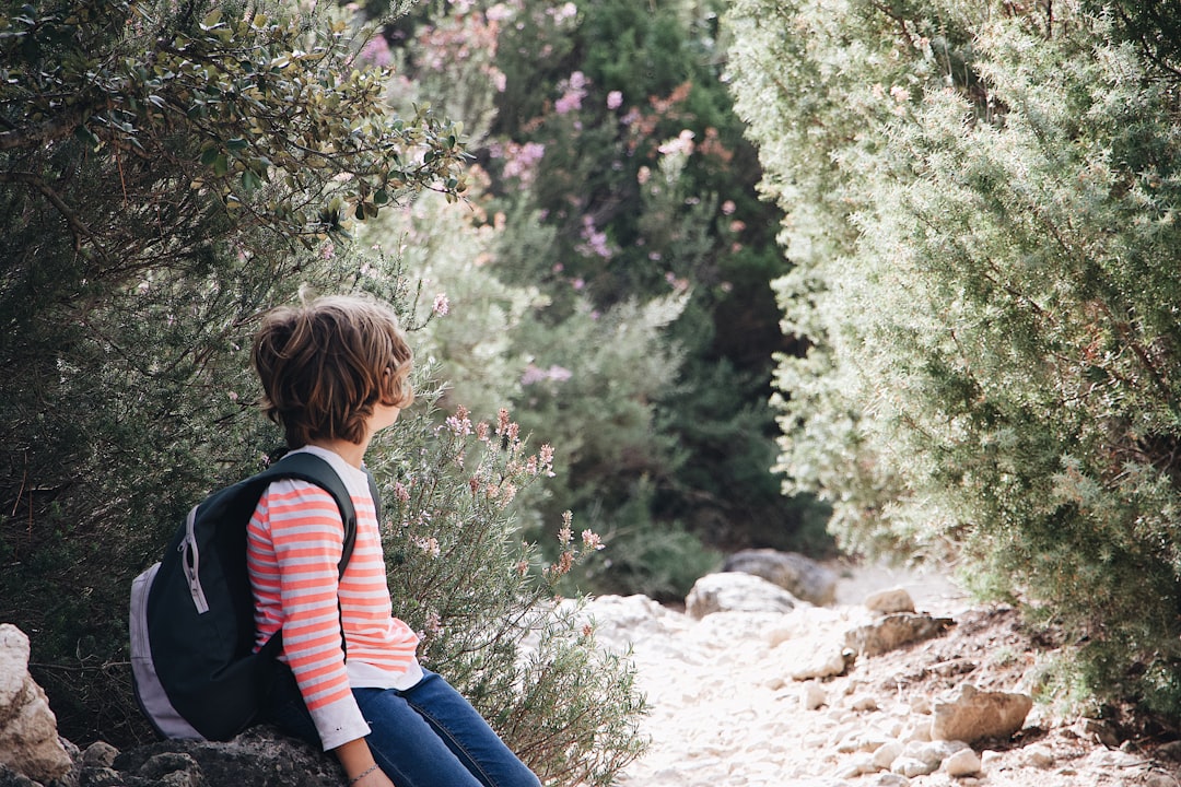 child carrying backpack sitting on a rock