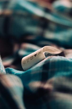 A close-up shot of a clothing label showing various laundry symbols. The background is a blurred fabric pattern in shades of blue and black.