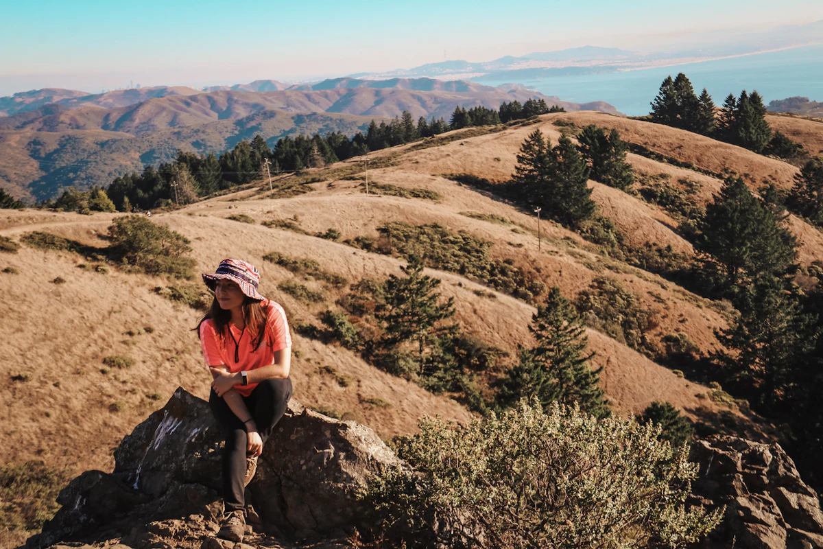 A hiker resting on a rock above golden hills and pines near Mill Valley