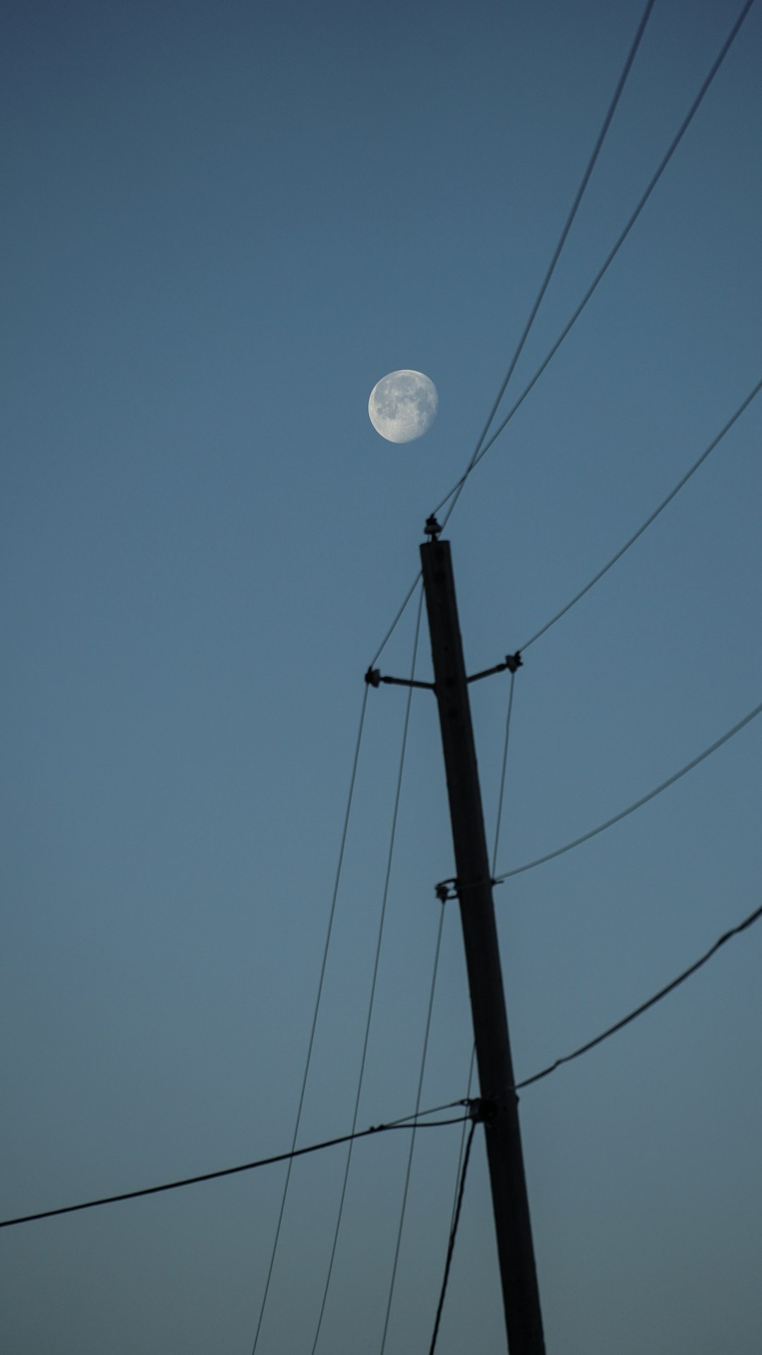 electric post under a full moon in a calm blue sky