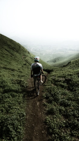 A mountain biker riding along a rugged trail at sunrise, with mist rising from the forest below.