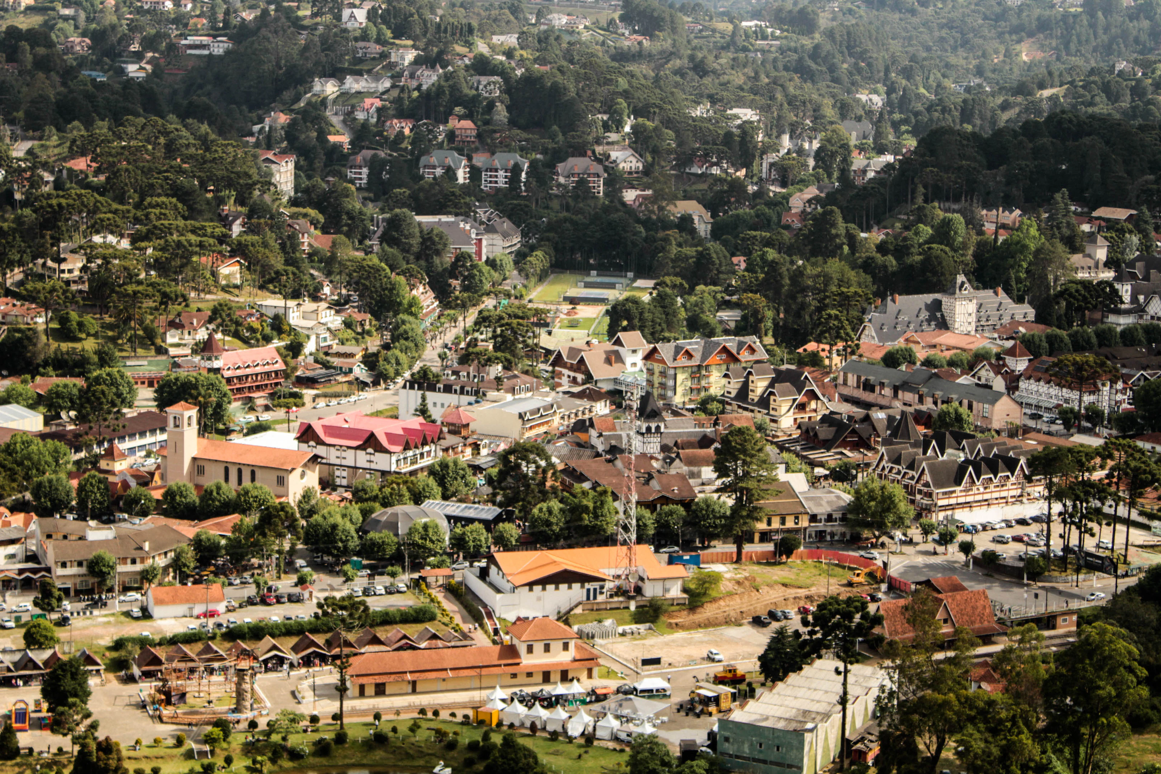 Aerial view of Campos do Jordão, a mountain town with alpine-style rooftops among green hills.