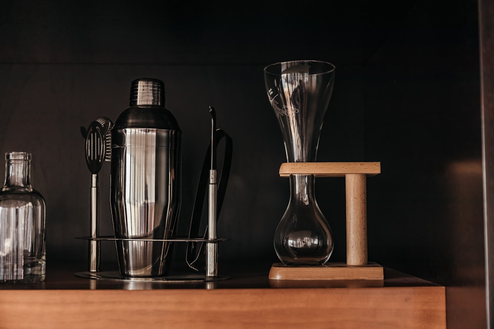 clear glass decanter on brown wooden stand beside stainless steel cocktail shaker