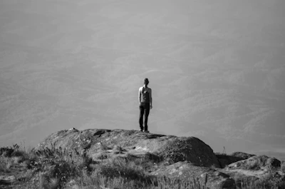 A cinematic black and white portrait of a lone explorer gazing into a vast mountain landscape at dusk.
