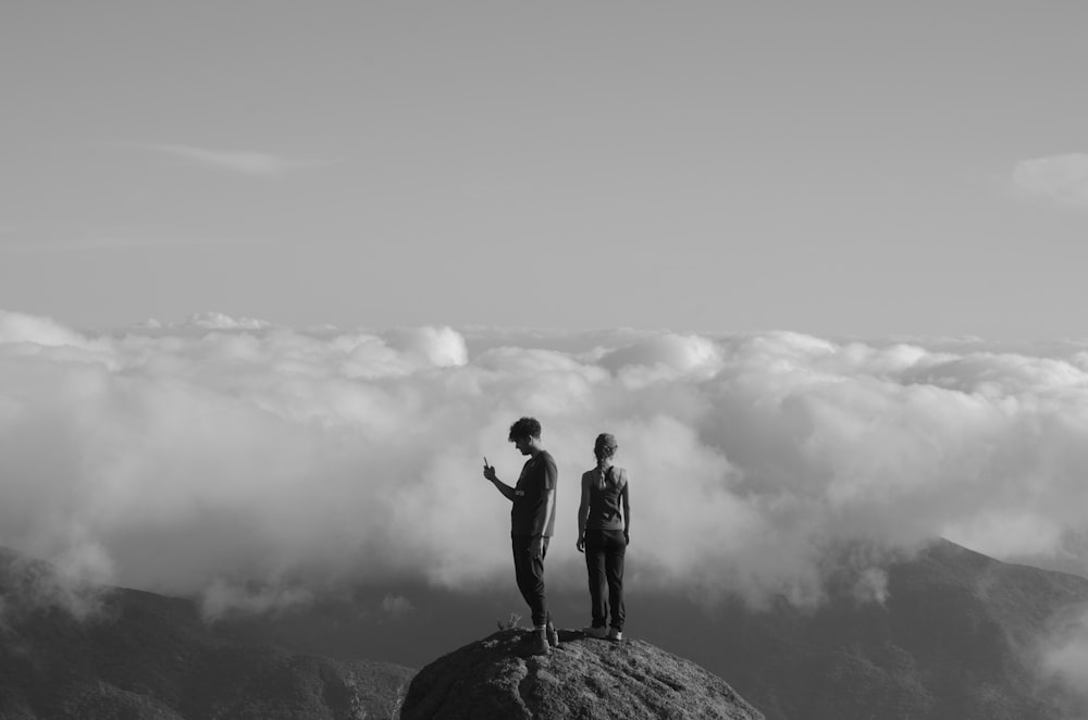 grayscale photo of two men standing on cliff