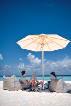 three person sitting on the sand with umbrella