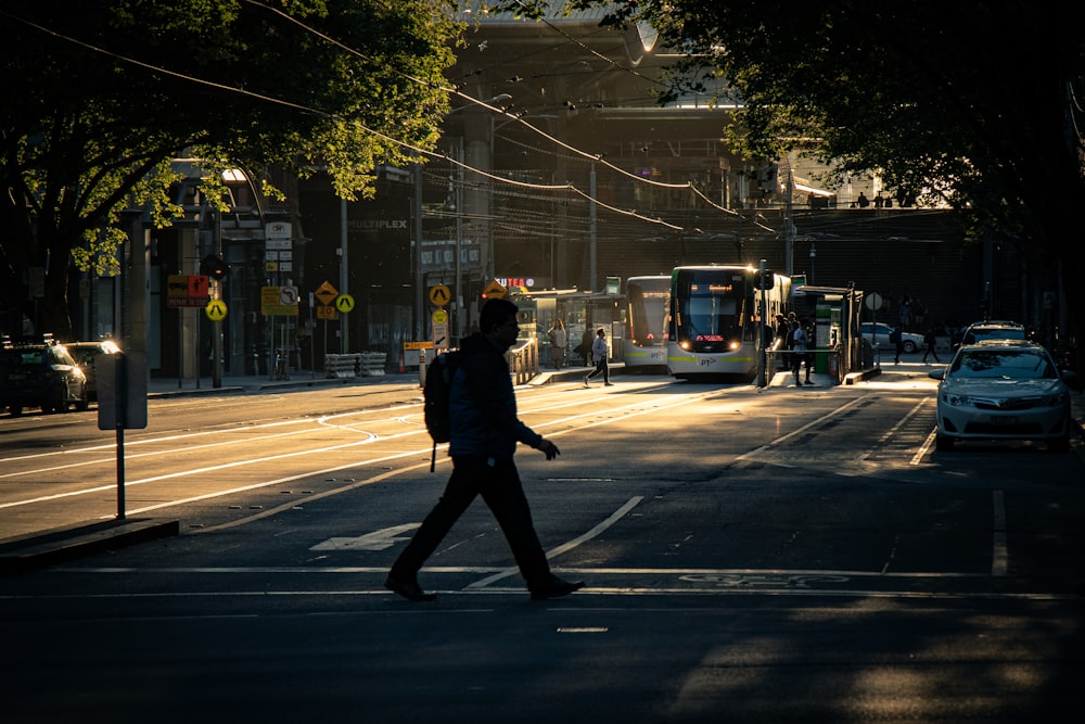 man crossing on pedestrian lane and different vehicles on road during daytime