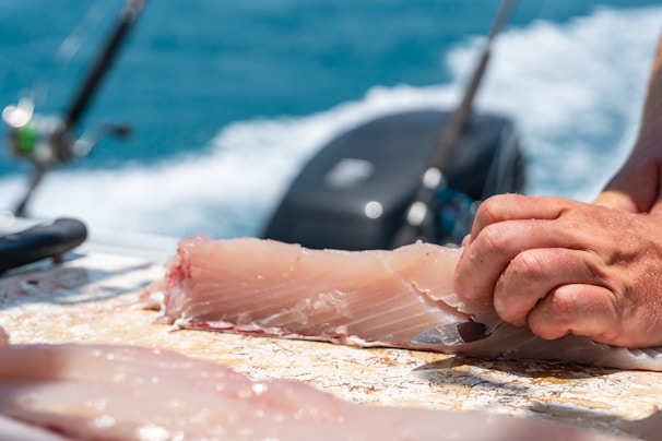 Close-up of skilled hands filleting fresh fish against a white and blue backdrop.