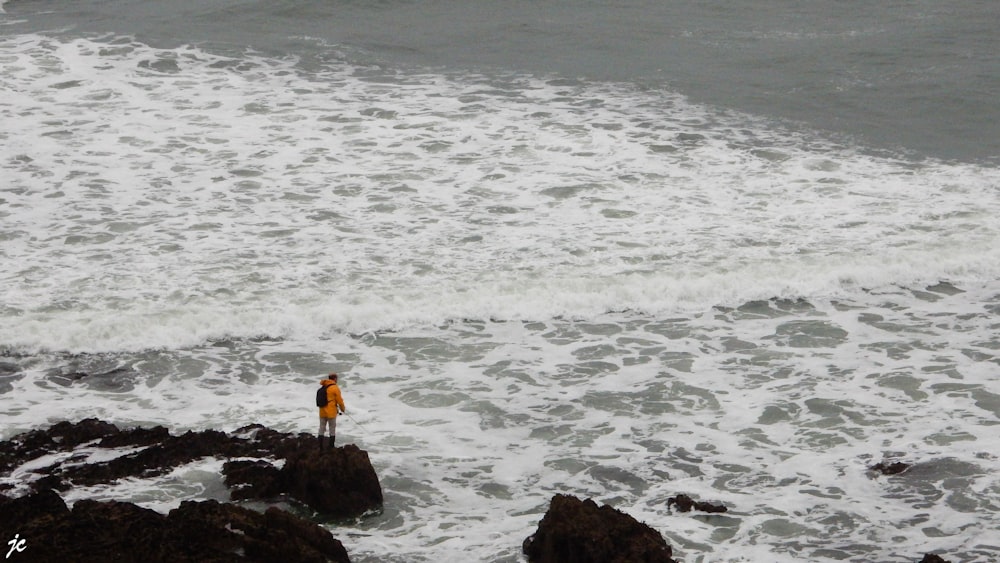 person standing on rocks beside body of water